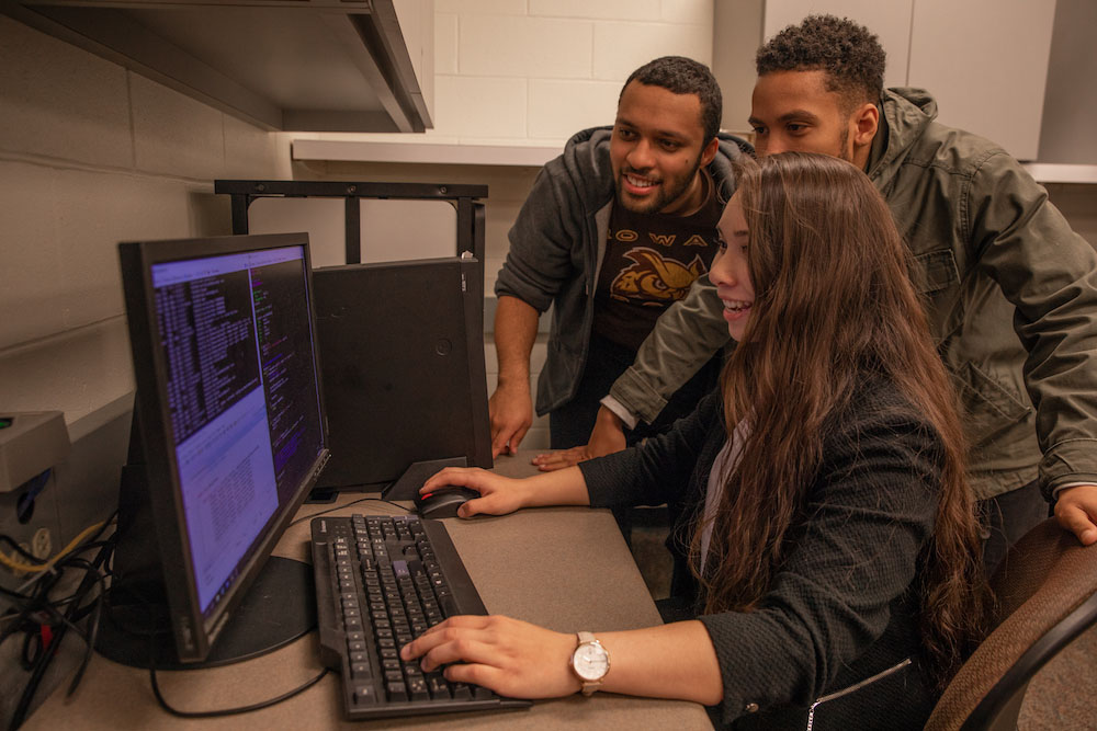Three computer science students at Rowan University look at a desktop computer screen.